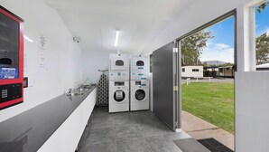 Un moderno cuarto de lavandería con dos lavadoras apiladas, una máquina expendedora de helado rojo y un amplio ventanal con vistas al exterior.