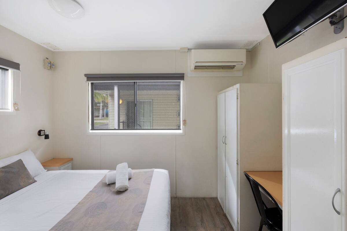 Une chambre comprenant un lit, un bureau, une armoire, une fenêtre et un appareil de climatisation.