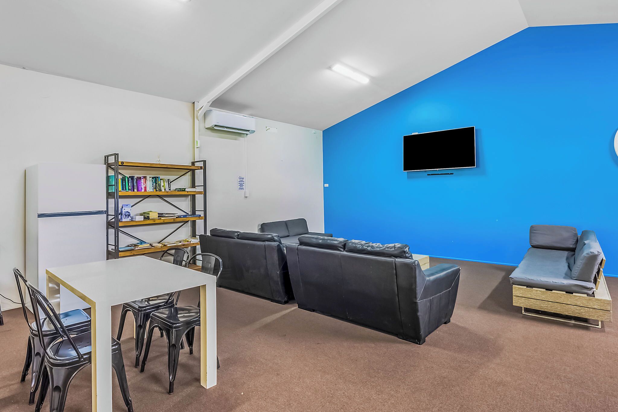 Een moderne kamer met een witte tafel, zwarte stoelen, een boekenkast, een blauwe accentmuur, een flatscreen televisie en een bank.