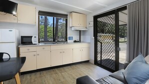 Cocina compacta con microondas, lavamanos y armarios, zona de comedor con mesa y sillas, y puerta corrediza de vidrio que da a un espacio exterior.