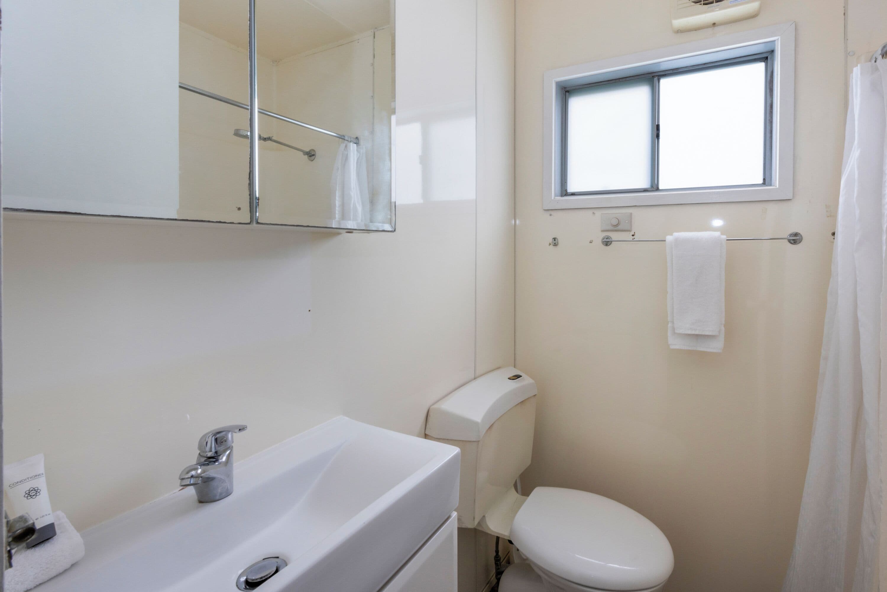 A bathroom with a sink, mirror, toilet, and window.
