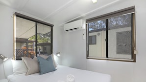 Habitación de hotel con cama, dos almohadas, toalla enrollada, unidad de aire acondicionado y ventana con vistas.