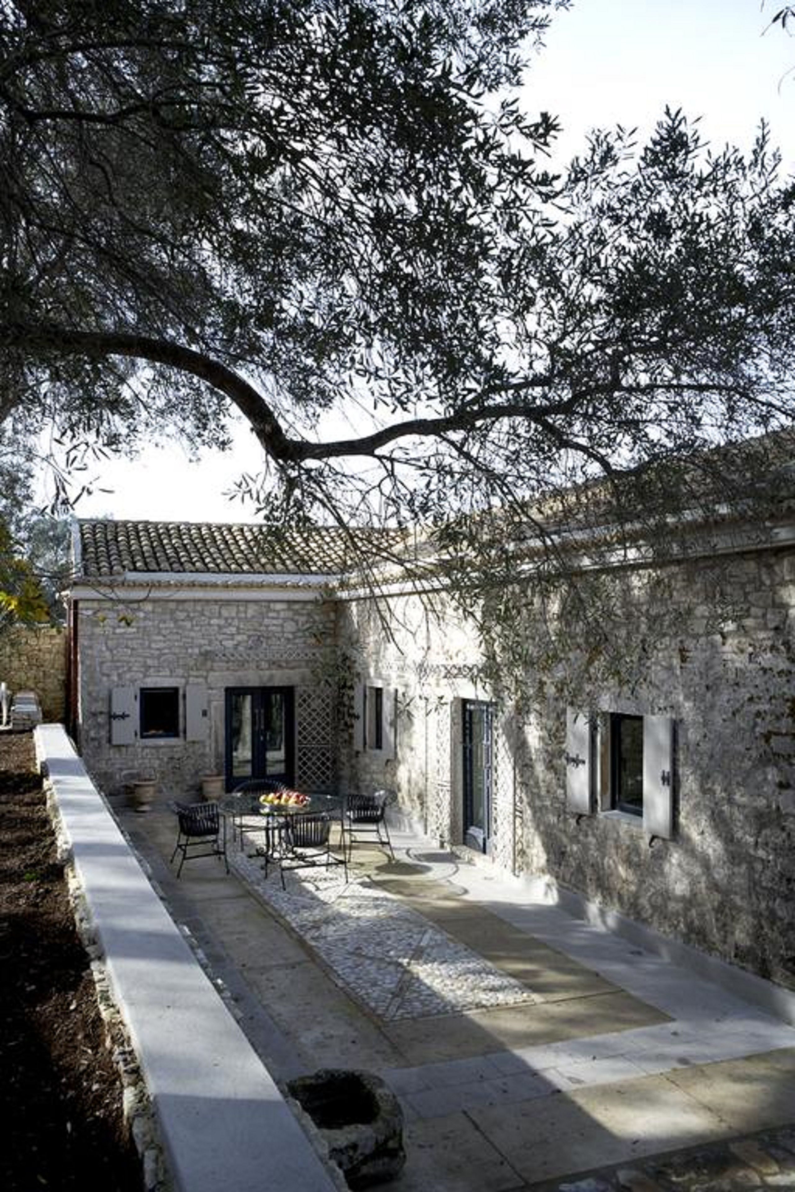A stone building with a tiled roof, a paved courtyard, and a table with chairs.