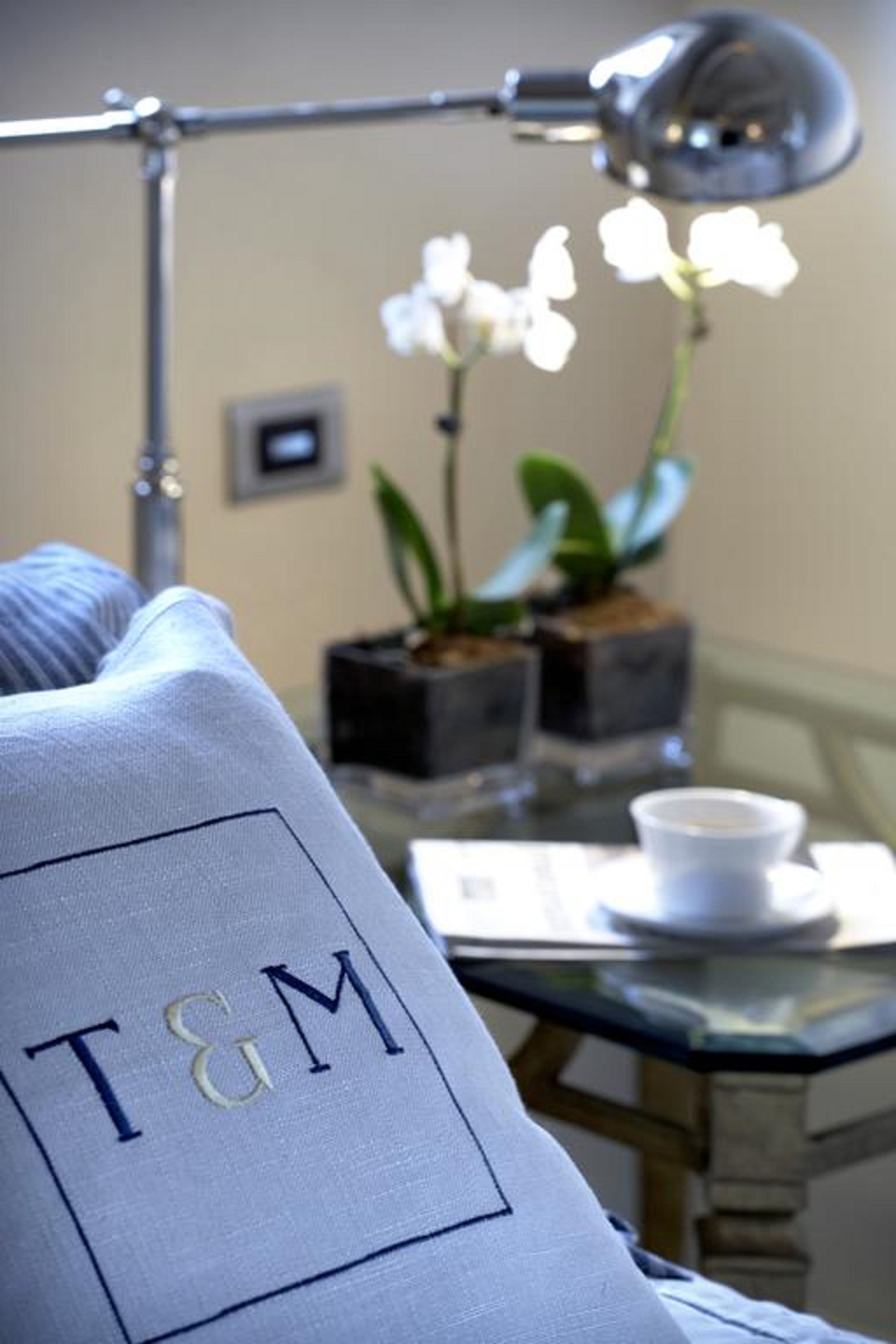 Een keurig opgeruimde hotelkamer met een kussen waarop de initialen 'T&M', een tafel met kop en schotel, en een potorkidee.