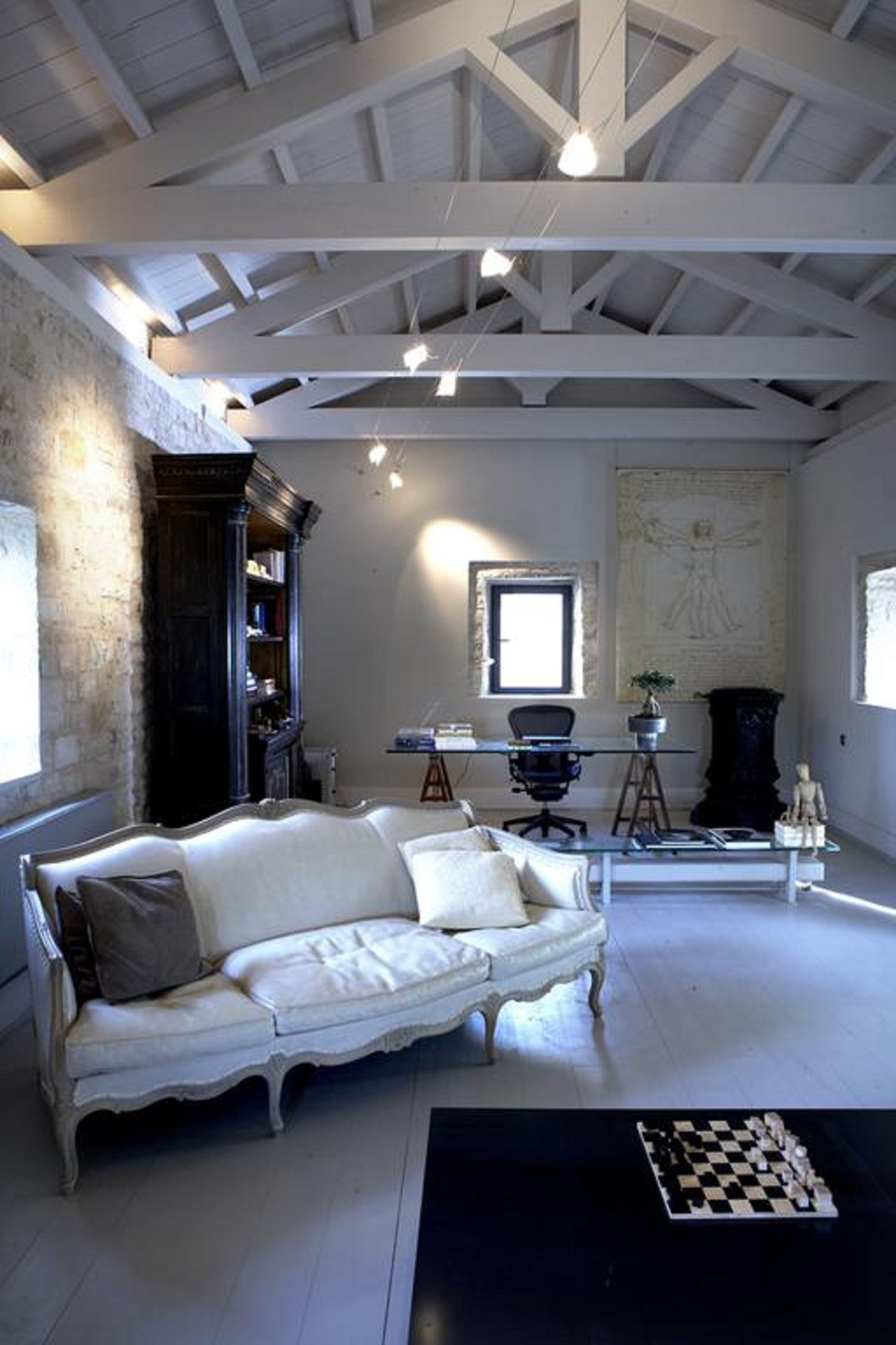 A spacious room with a white sofa, a desk with a computer, a bookshelf, and a chessboard on the floor.