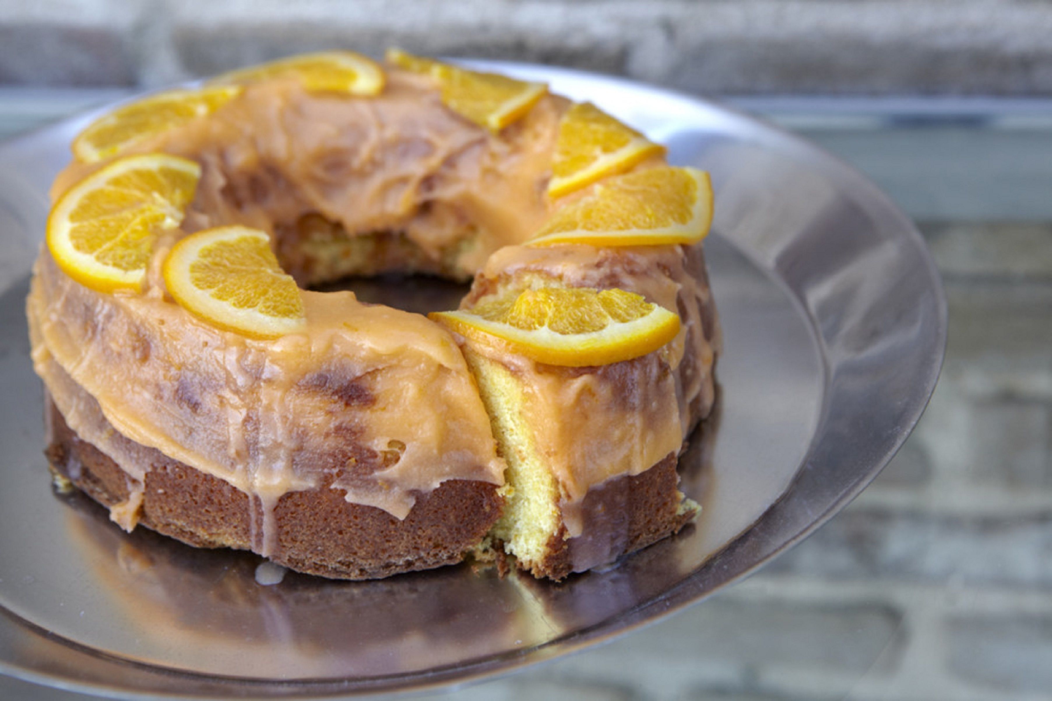 A bundt cake with orange slices on a metal plate.