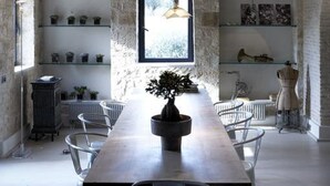 A dining area with a long table, chairs, a potted plant, and shelves with decorative items. - Torri E Merli Hotel by GHH (Paxos)