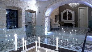 An interior with stone arches, a glass table with candles, and a chandelier. - Torri E Merli Hotel by GHH (Paxos)