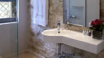 A bathroom with a stone wall, a glass shower enclosure, a white sink, and a large mirror.