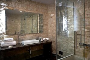 A modern bathroom with a stone wall, a glass shower enclosure, and a marble sink. - Torri E Merli Hotel by GHH (Paxos)