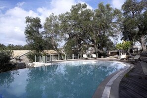 A swimming pool with lounge chairs and trees in the background. - Torri E Merli Hotel by GHH (Paxos)