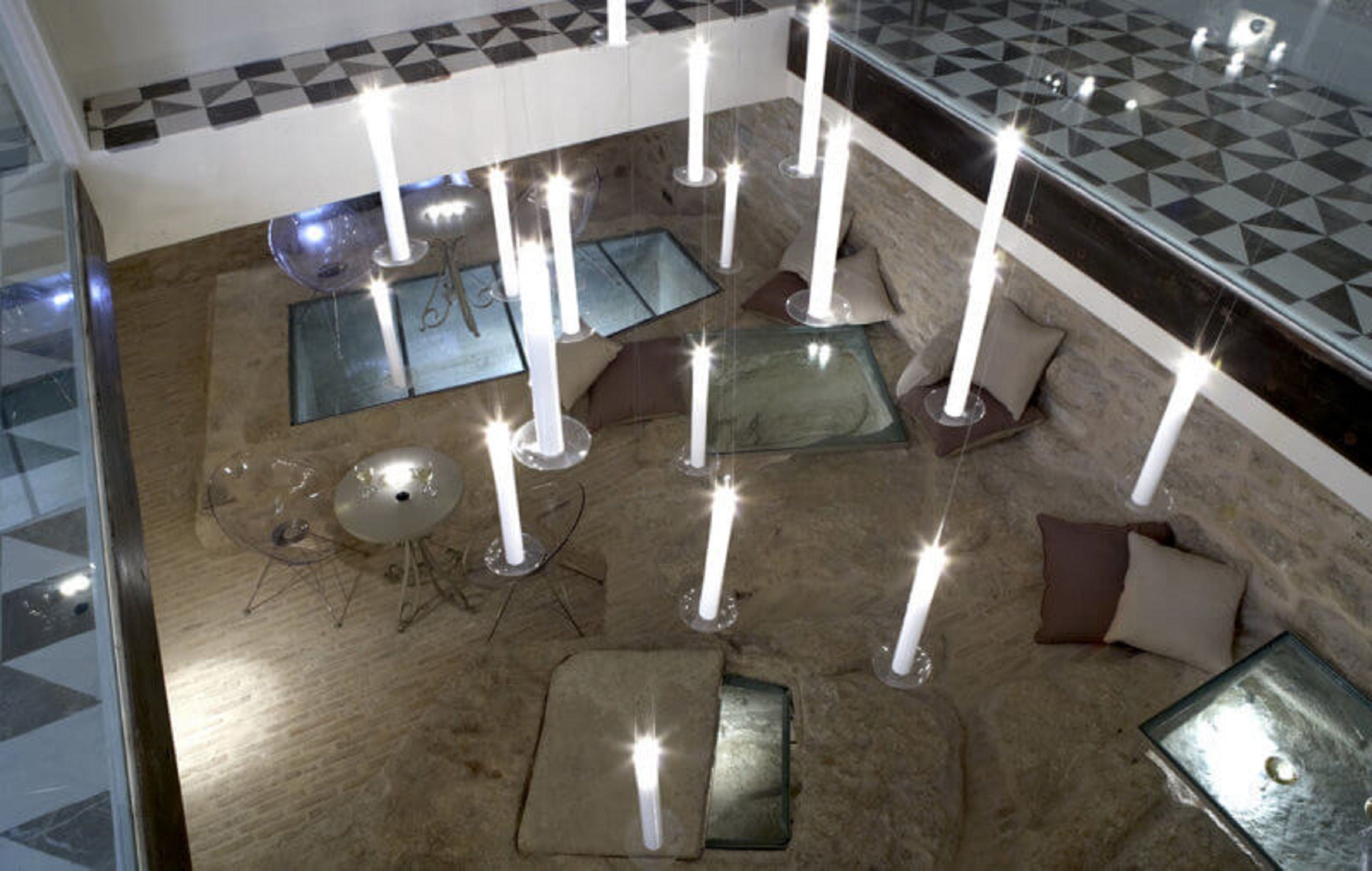 Un hall d’entrée avec un sol à carreaux, plusieurs espaces aménagés pour s’asseoir et plusieurs bougies posées sur des supports.