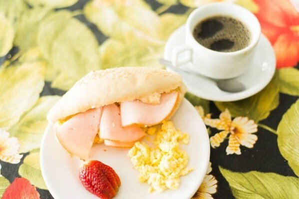 A plate with scrambled eggs, a slice of ham, and a strawberry on a floral tablecloth.