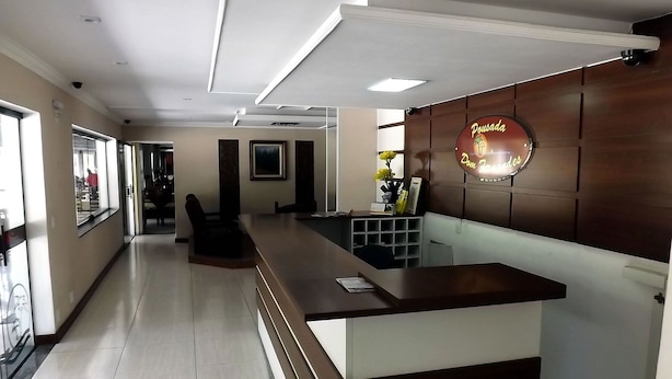 A reception area with a wooden reception desk, a wall-mounted sign, and a seating area with chairs. - Pousada Dom Fernandes (Cabo Frio)