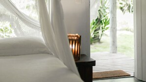 Quarto com cama, mesa de cabeceira e luminária, e vista para o verde lá fora.