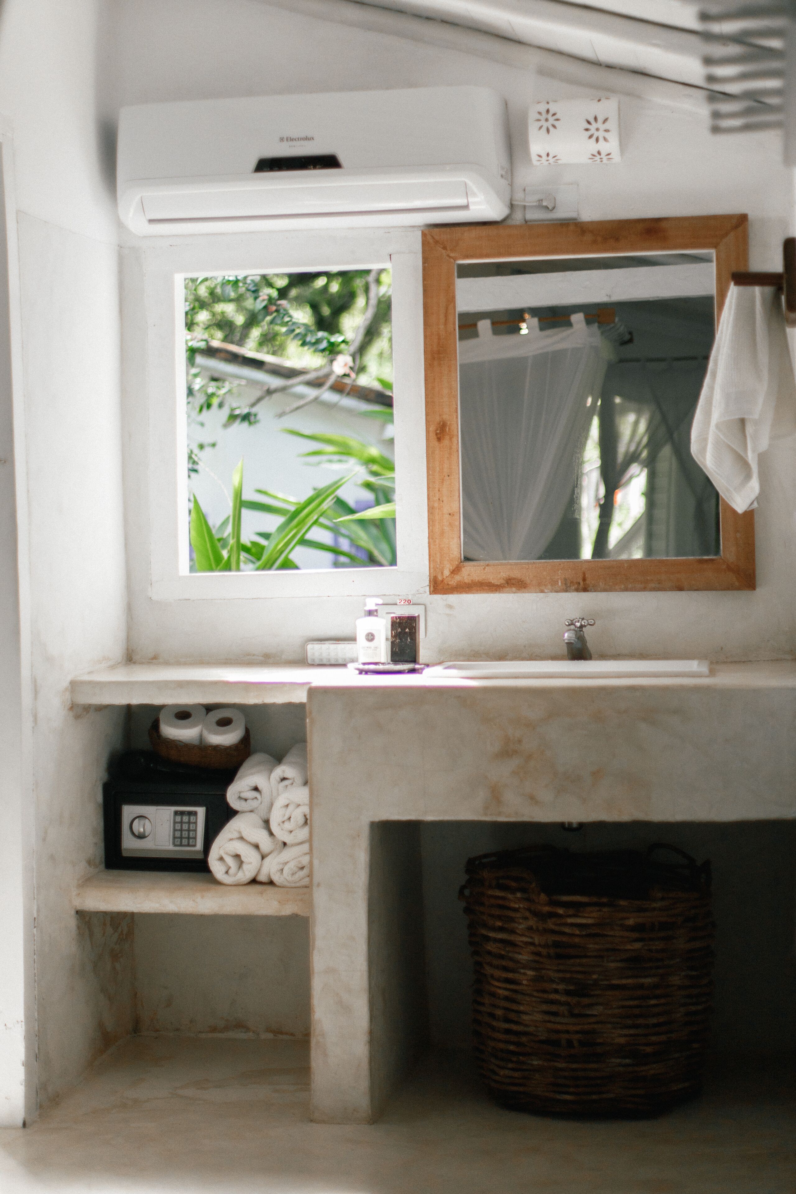 Une salle de bain avec une fenêtre, un miroir, un lavabo, un porte-serviettes et un panier.