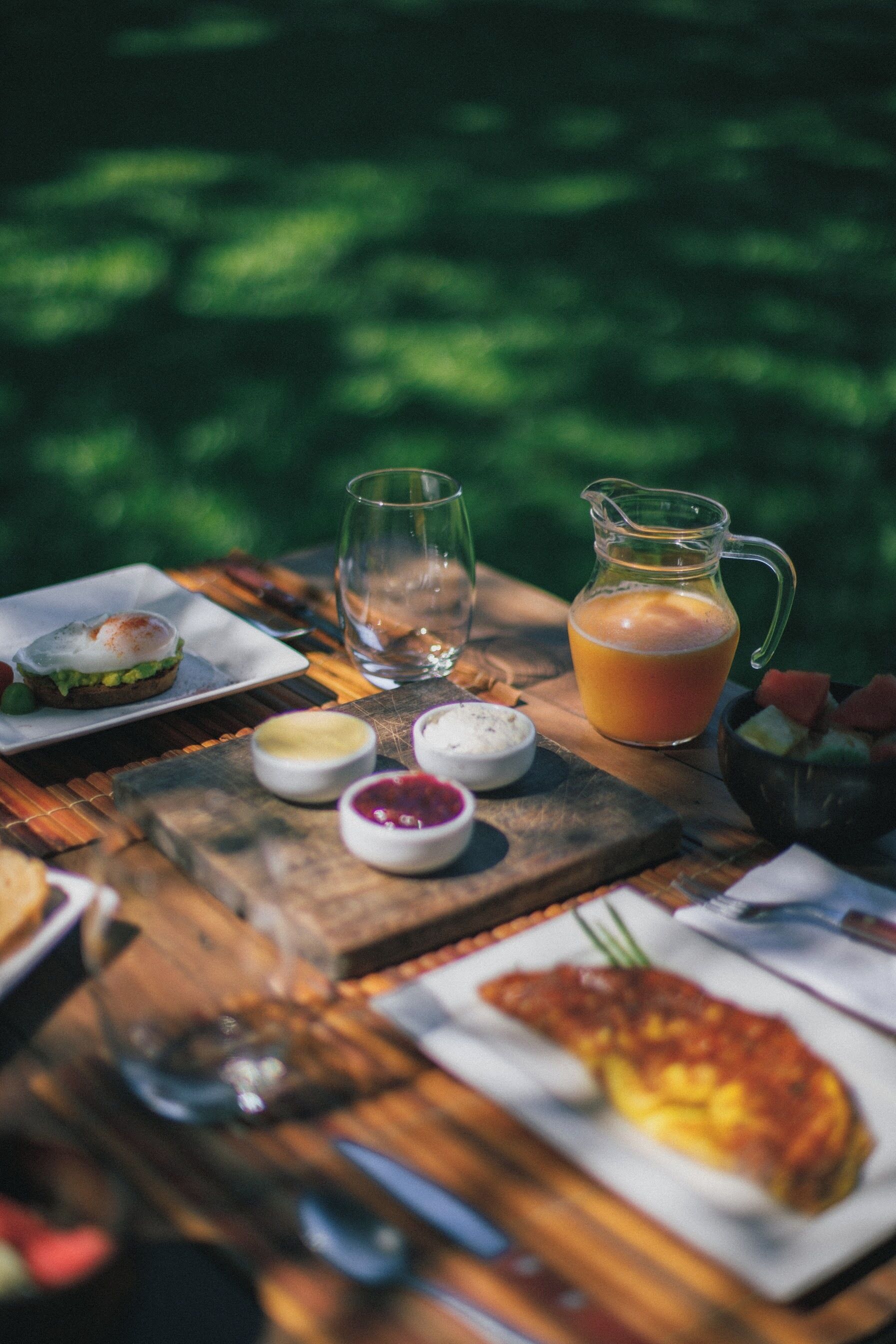 A wooden table with a meal setup including a plate with a sandwich, a glass of juice, and a pitcher of orange juice.