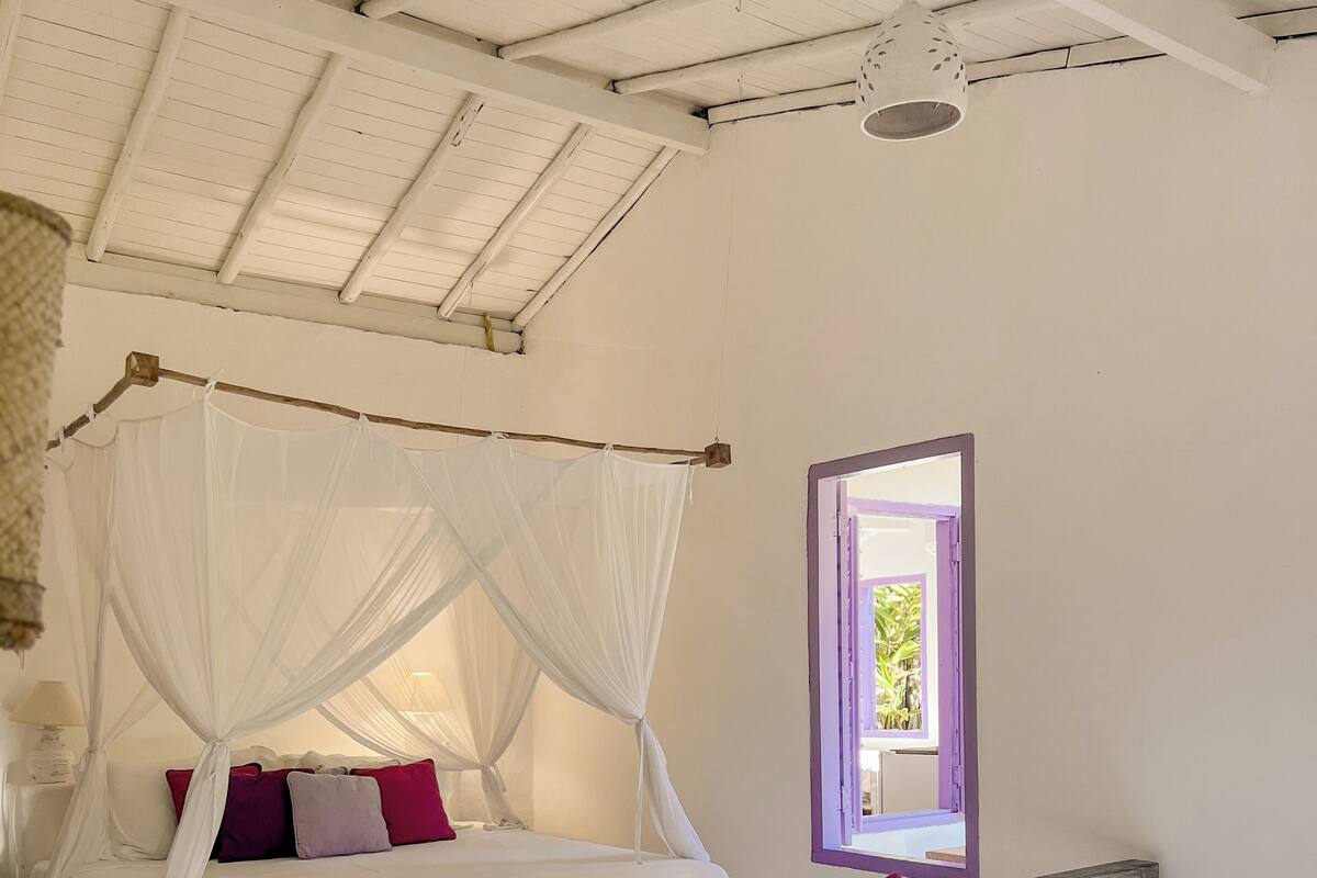Ein Schlafzimmer mit zwei Betten, einem hölzernen Kopfteil, einem Moskitonetz und einem Fenster mit Blick.