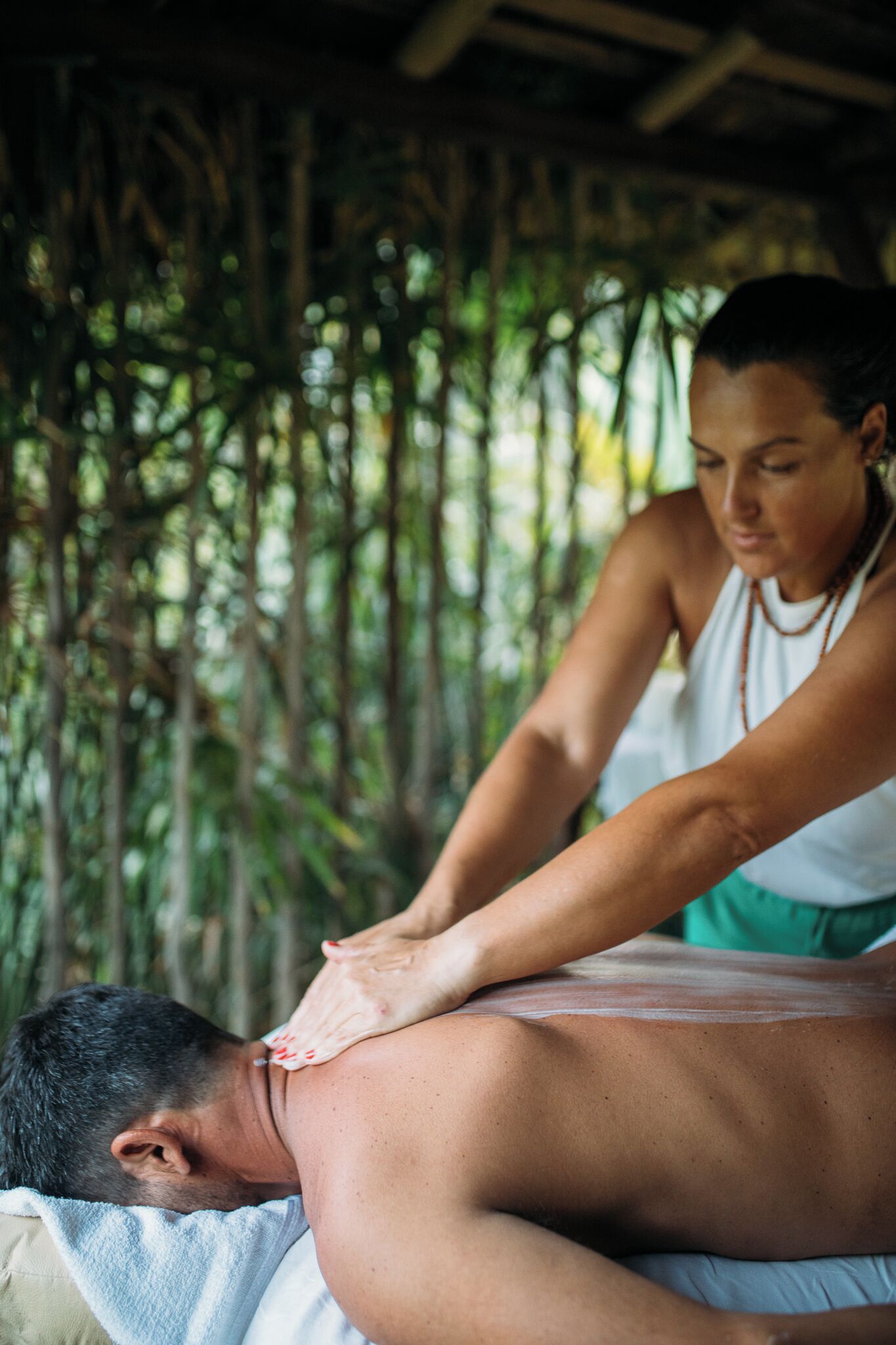 A person receiving a massage in a room with a wooden ceiling and a view of greenery outside.