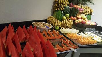 Un buffet con diversi tipi di frutta e verdura, tra cui anguria, papaya, banane, mele e arance.