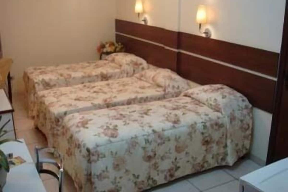 A hotel room with two beds, a wooden headboard, wall-mounted lamps, and a small table with a chair.