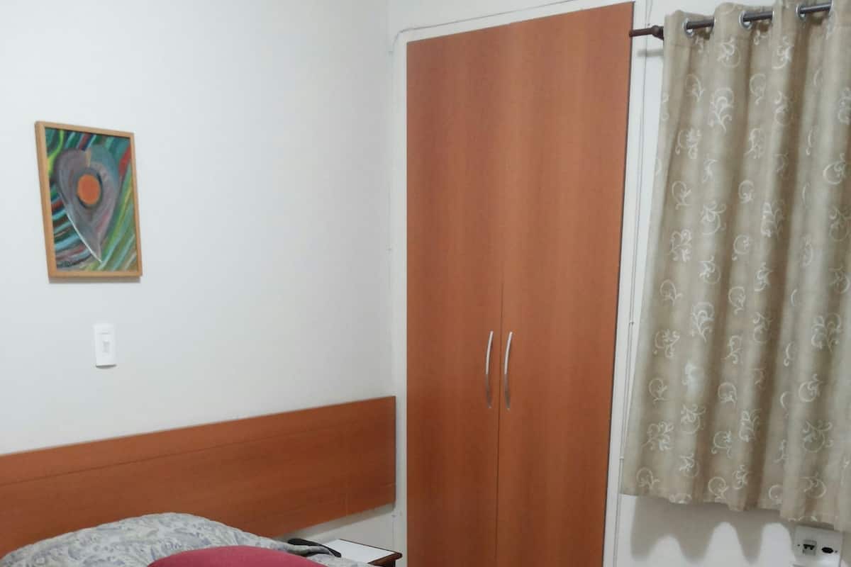 A bedroom with a bed, a wardrobe, a painting, and a curtain.