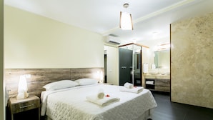 Une chambre d’hôtel avec un grand lit, une table de chevet, un miroir et une salle de bain visible à travers une porte ouverte.