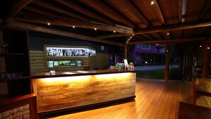 Un espace bar en bois, doté d’un comptoir, d’étagères et d’une vitrine, probablement situé dans un hôtel ou un complexe touristique.