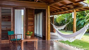 Une véranda en bois, avec un hamac, une table agrémentée d’un panier de fleurs et une chaise.