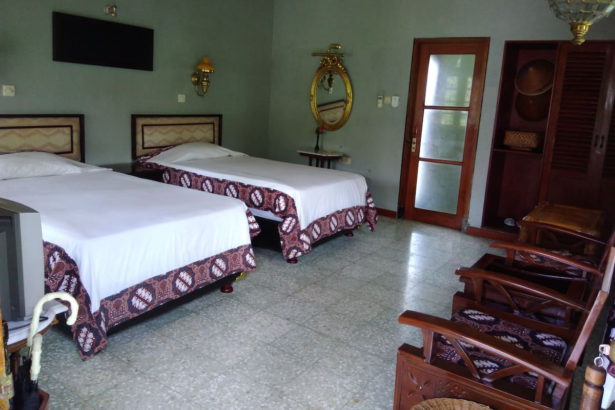 A hotel room with two beds, a television, a wooden cabinet, and a mirror.