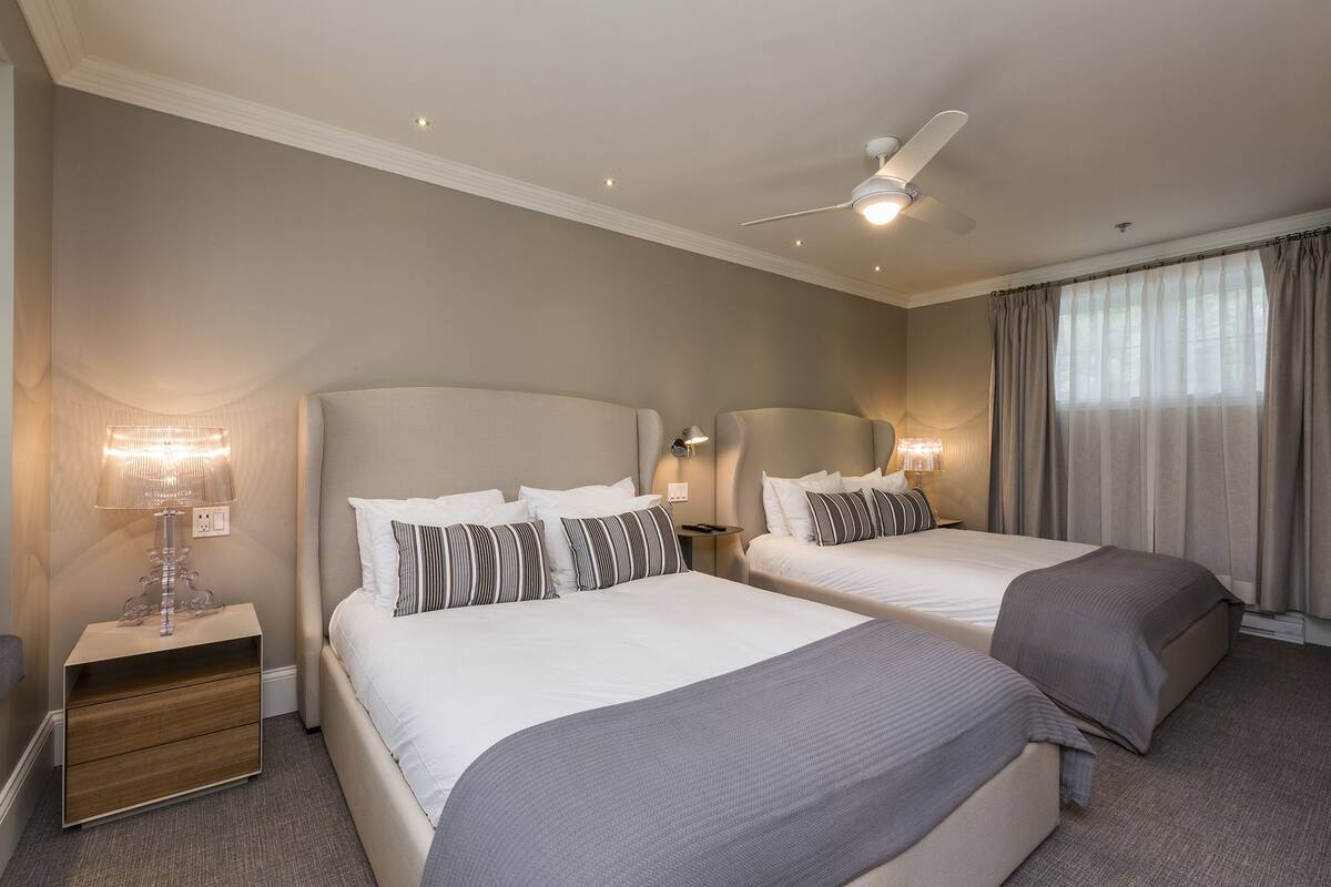 A hotel room with two beds, a ceiling fan, bedside lamps, and a nightstand.