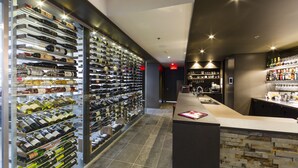 A wine cellar with numerous wine bottles on shelves, a bar area with a counter, and a modern interior design. - Chez Truchon (La Malbaie)