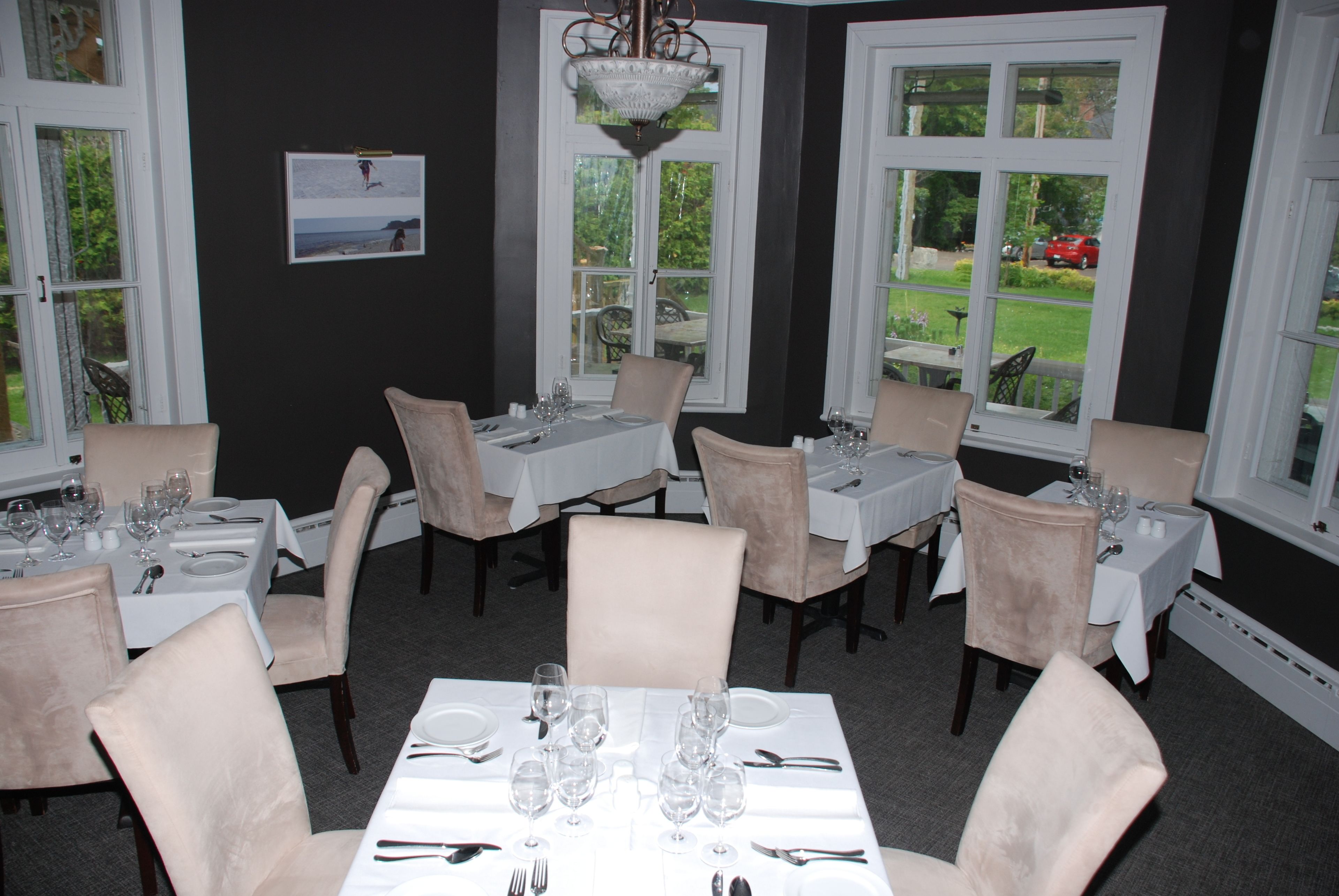 Un espace repas avec plusieurs tables dressées pour le repas, des chaises et une vue sur l’extérieur grâce à de grandes fenêtres.