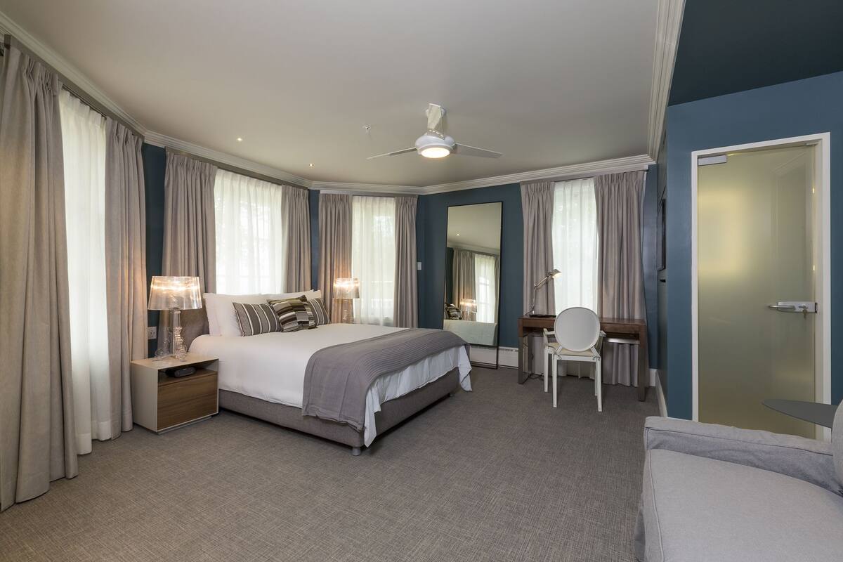 A modern hotel room with a large bed, a desk, a chair, and a ceiling fan.