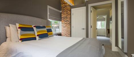 Un dormitorio moderno con una cama grande, una pared de ladrillo decorativa y un pasillo que conduce a otra habitación.