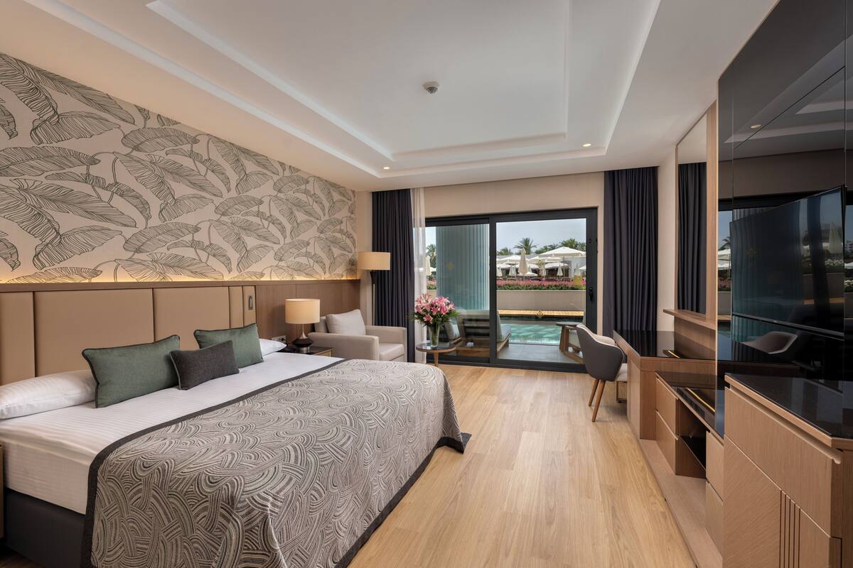 Une chambre d’hôtel moderne dotée d’un grand lit, d’un bureau, d’une télévision et d’un balcon aménagé avec du mobilier d’extérieur.