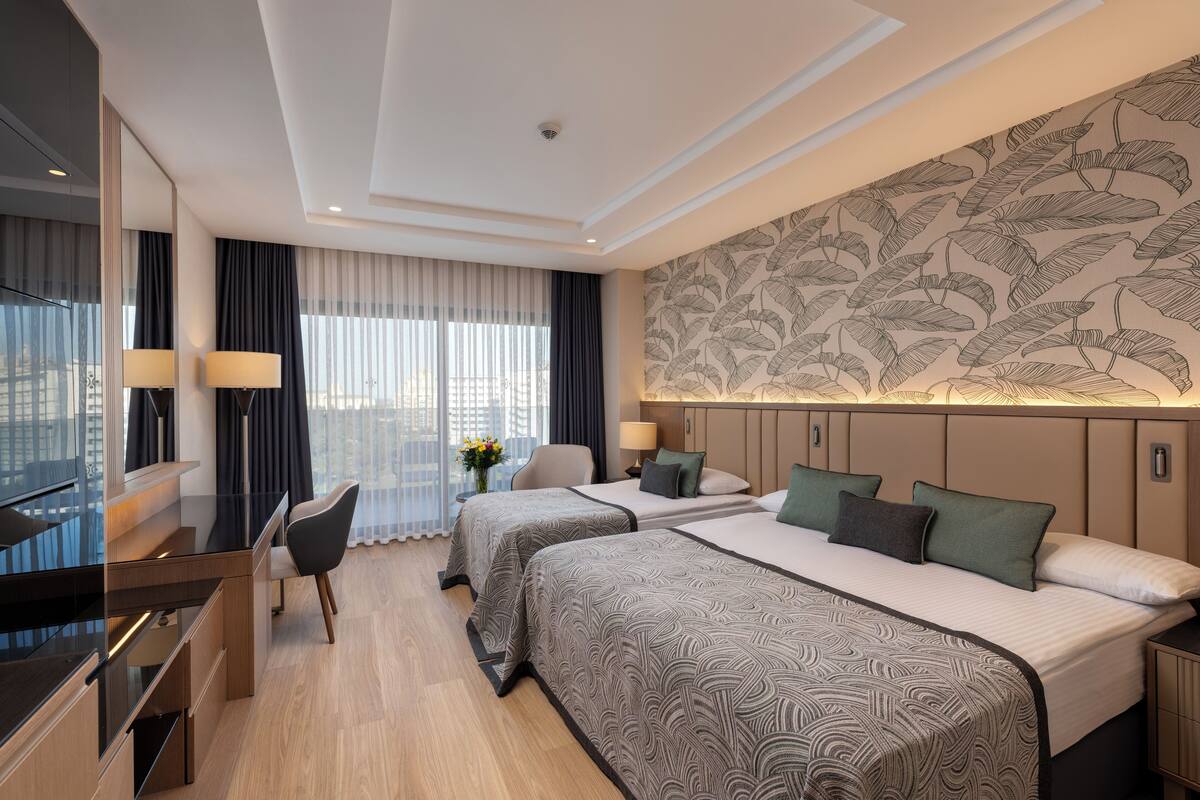 Une chambre d’hôtel avec deux lits, un bureau, une chaise et une grande fenêtre avec des rideaux.