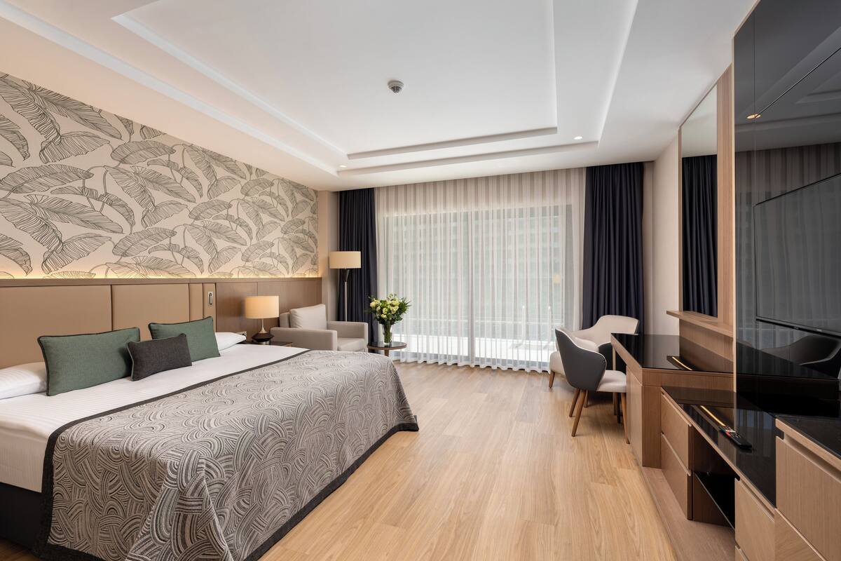 Une chambre d’hôtel avec un grand lit, un bureau avec une télévision, une chaise et une fenêtre avec des rideaux.
