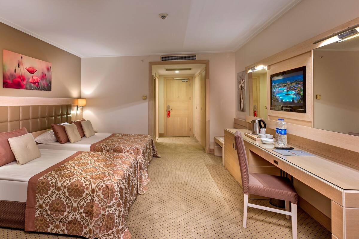 Une chambre d’hôtel avec deux lits, un bureau, une chaise, une télévision et une porte de salle de bain.