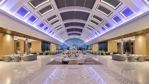 Un hall d’entrée spacieux agrémenté d’une composition florale centrale, de coins salon et d’un design de plafond moderne.