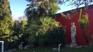 A garden with a statue, various plants, and a red wall. - 7MOTEL - SETTIMOTEL (Settimo Milanese)