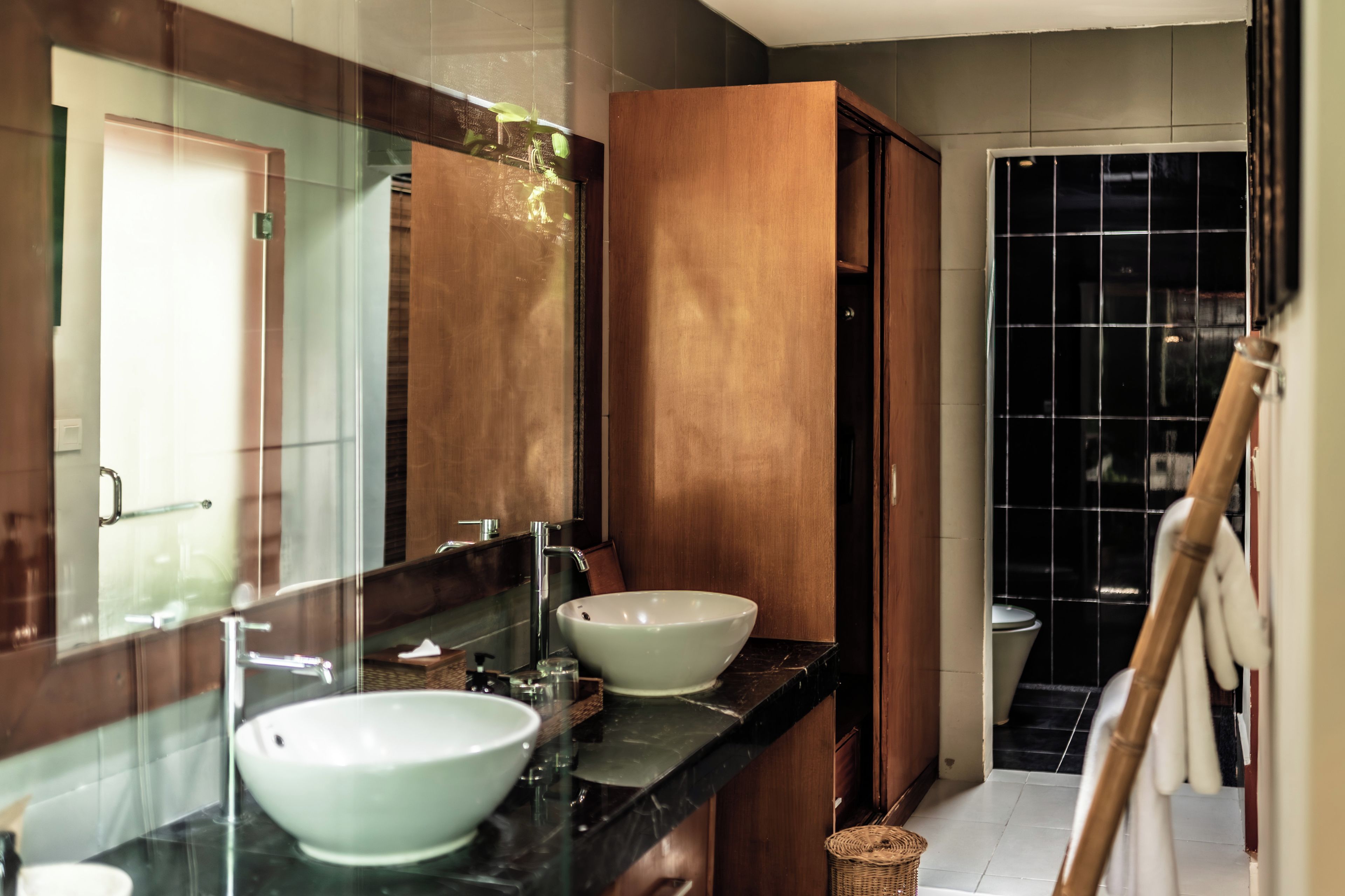 Un baño con un espejo grande, dos lavamanos, un armario de madera y una zona de ducha con azulejos.