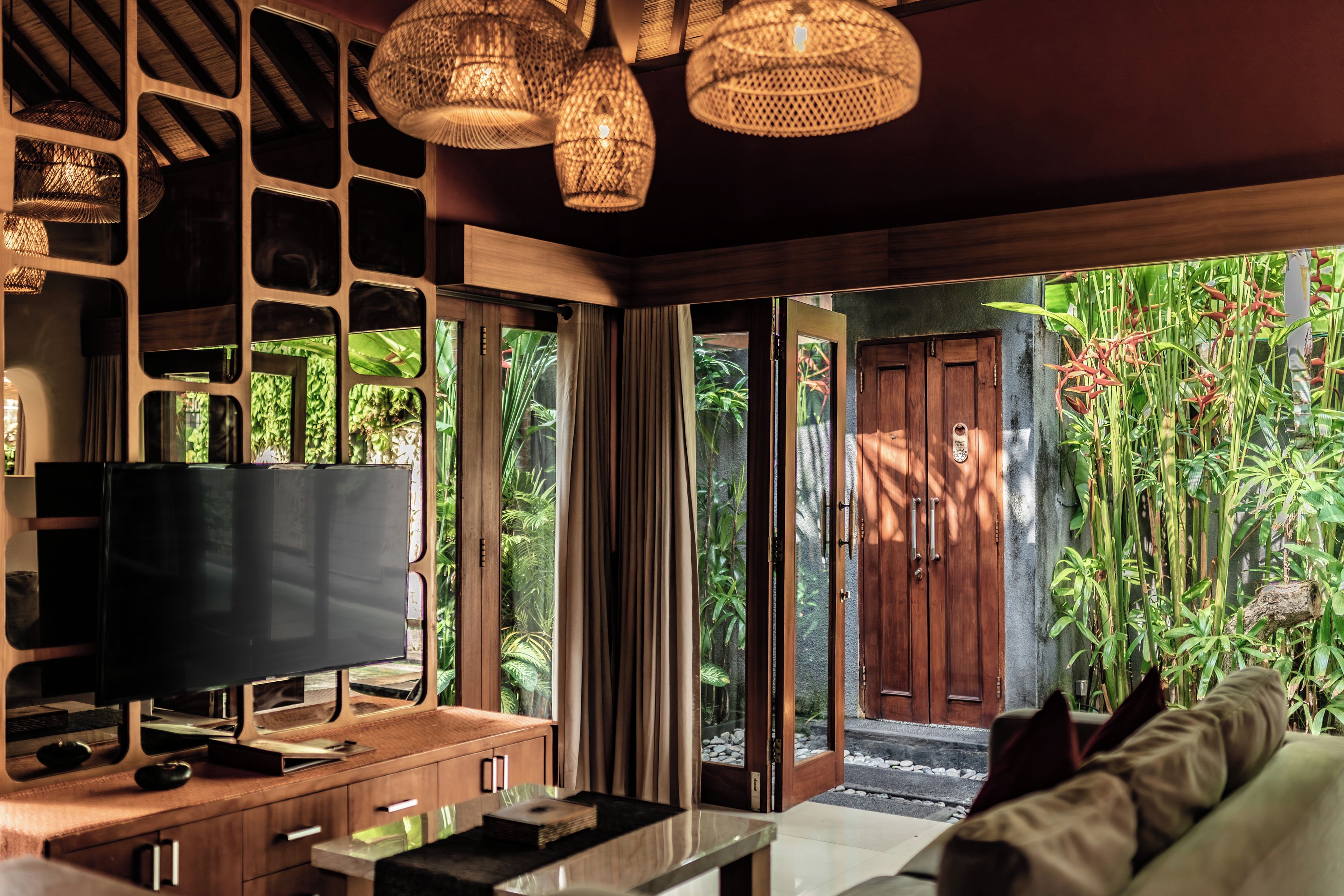 Ein modernes Wohnzimmer mit Flachbildfernseher, Holzmöbeln und einem großen Fenster mit Blick auf einen üppigen Garten.