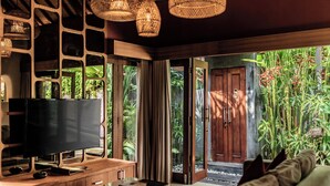 Un soggiorno moderno con televisore a schermo piatto, mobili in legno e una grande finestra con vista su un giardino rigoglioso.