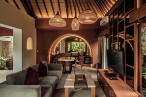 A modern living room with a sofa, coffee table, and TV. There is a kitchen in the background with a dining table and chairs. - Seminyak Sanctuary Villa by Ini Vie Hospitality (Legian)