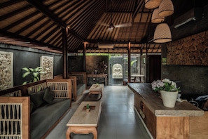 Une pièce spacieuse avec un plafond en bois, un espace salon central comprenant un canapé et des tables, et une grande statue de Bouddha en arrière-plan.
