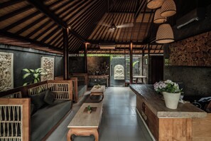 A spacious room with a wooden ceiling, a central seating area with a sofa and tables, and a large Buddha statue in the background. - Seminyak Sanctuary Villa by Ini Vie Hospitality (Legian)