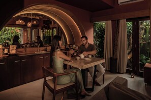 A modern kitchen with a curved ceiling, a dining table, and a large window with curtains. - Seminyak Sanctuary Villa by Ini Vie Hospitality (Legian)