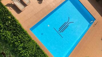 Una piscina rectangular con un borde de baldosas, rodeada de un seto cuidado y algunas sillas de descanso.