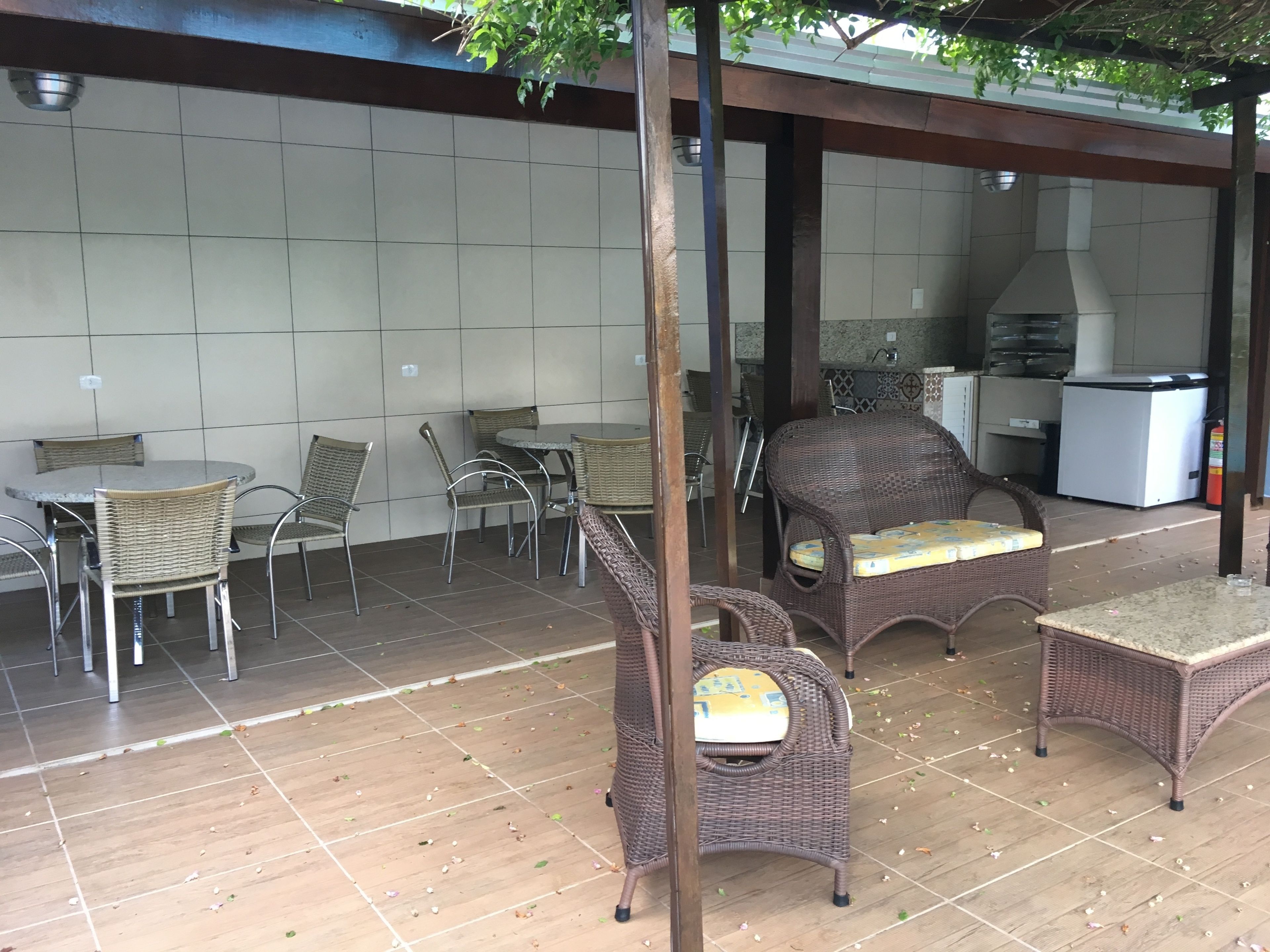 Un patio exterior con mobiliario de mimbre, piso de baldosas y una zona de cocina al fondo.